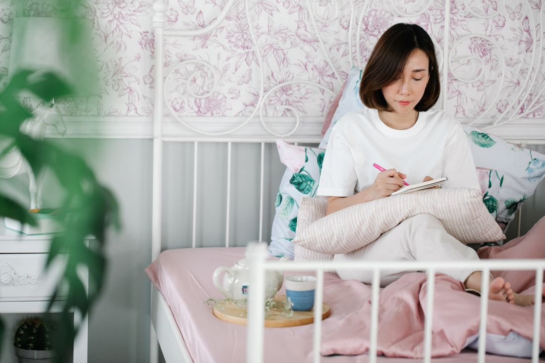 A woman writing thoughtfully in a journal in a cozy room