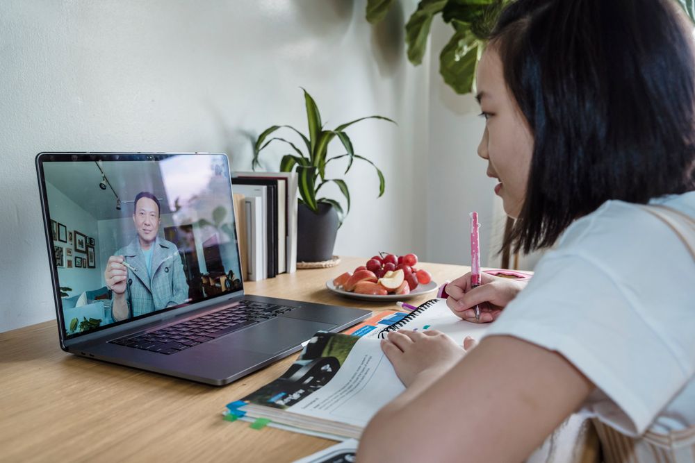 A young person learning online on a laptop and taking notes