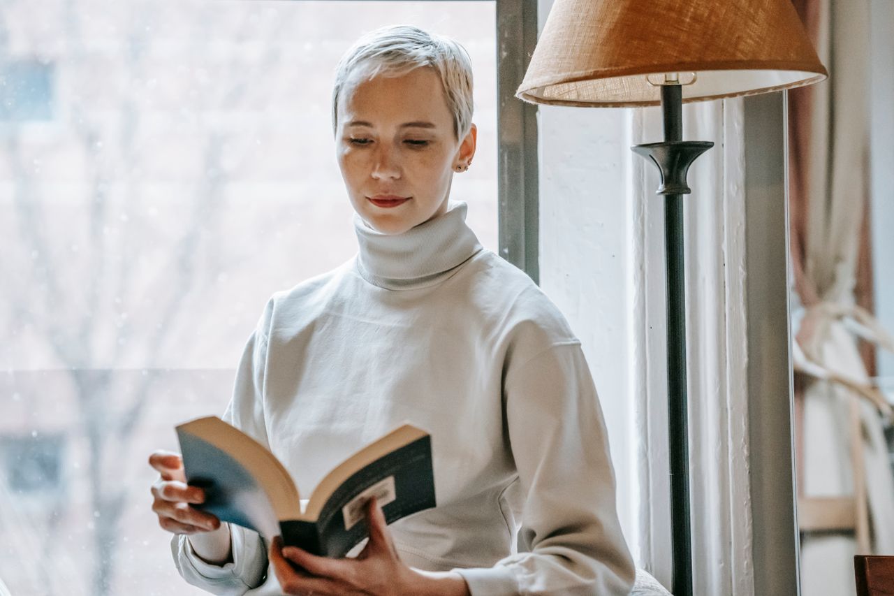 A person reading an open book beside a sunlit window